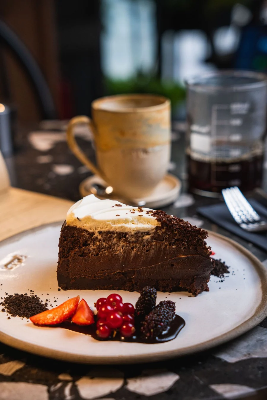 A generous slice of chocolate cake with cream and fresh berries in a café